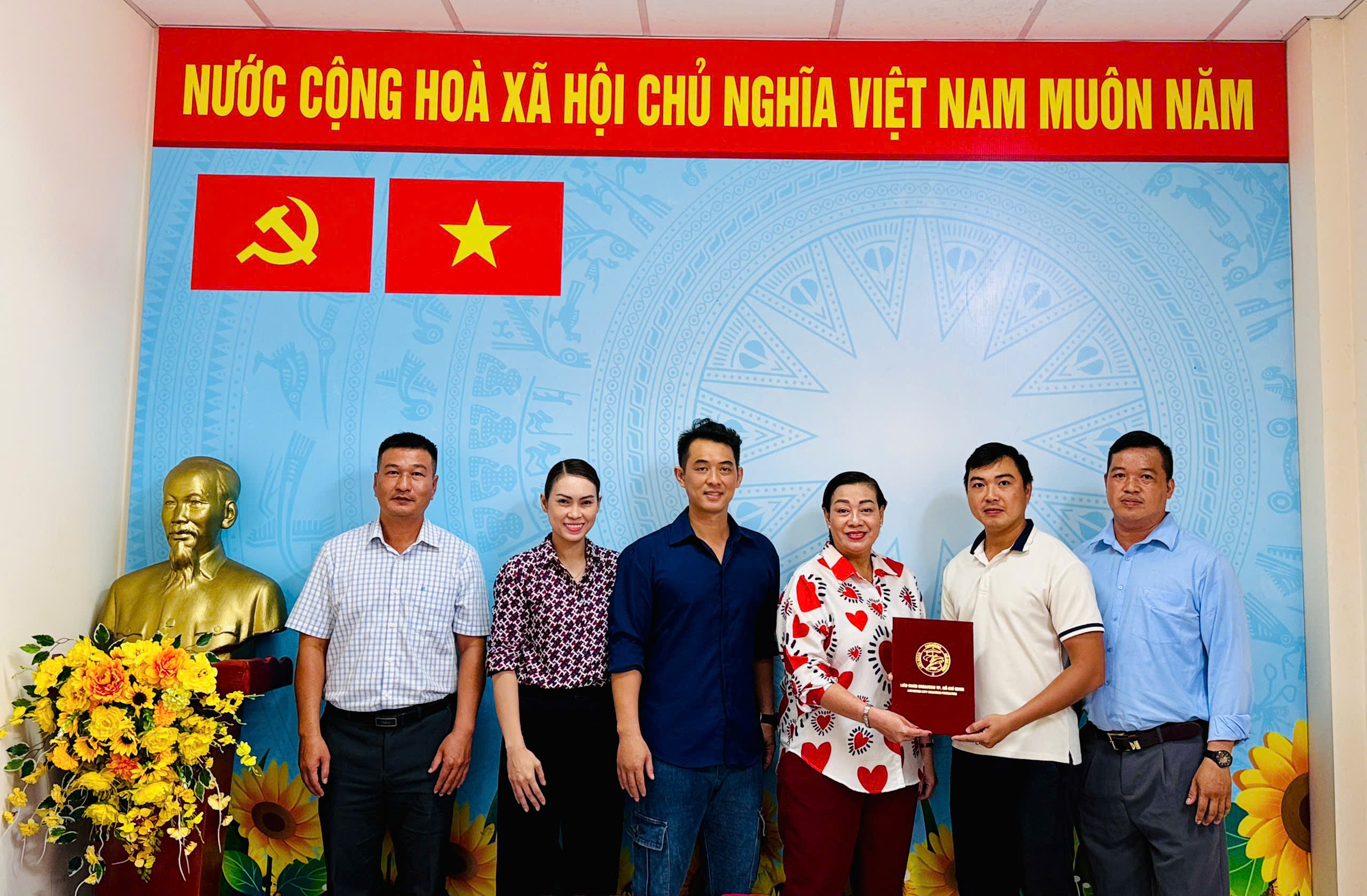 Các thành viên Ban Phát triển thành tích cao đứng chụp ảnh tại Hội nghị; hai người ở giữa cầm một bìa hồ sơ màu đỏ của HKF.