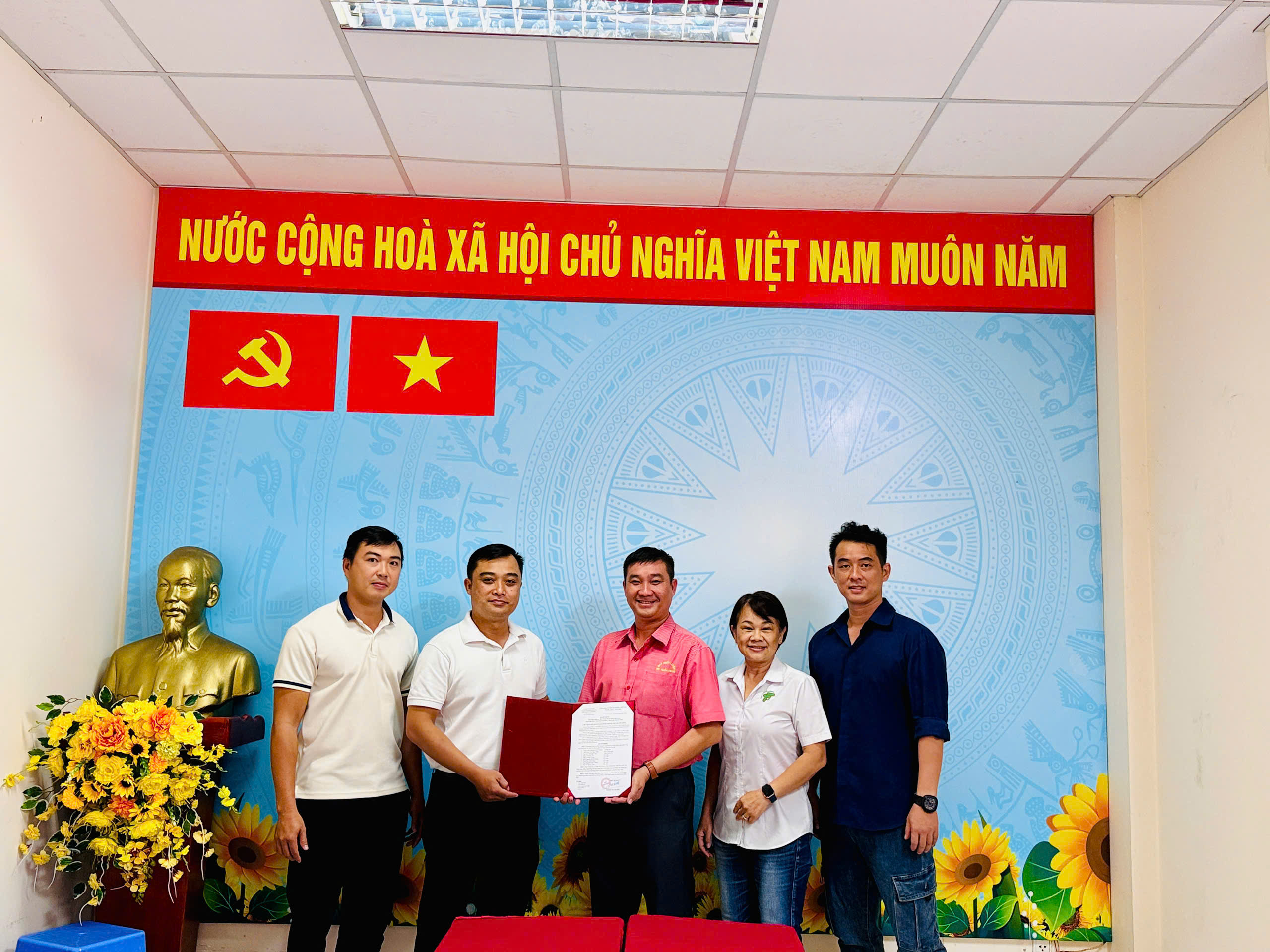 Đại diện Ban Kinh tế, Tài trợ chụp ảnh tại Hội nghị; hai người ở giữa cầm hồ sơ màu đỏ có văn bản bên trong.