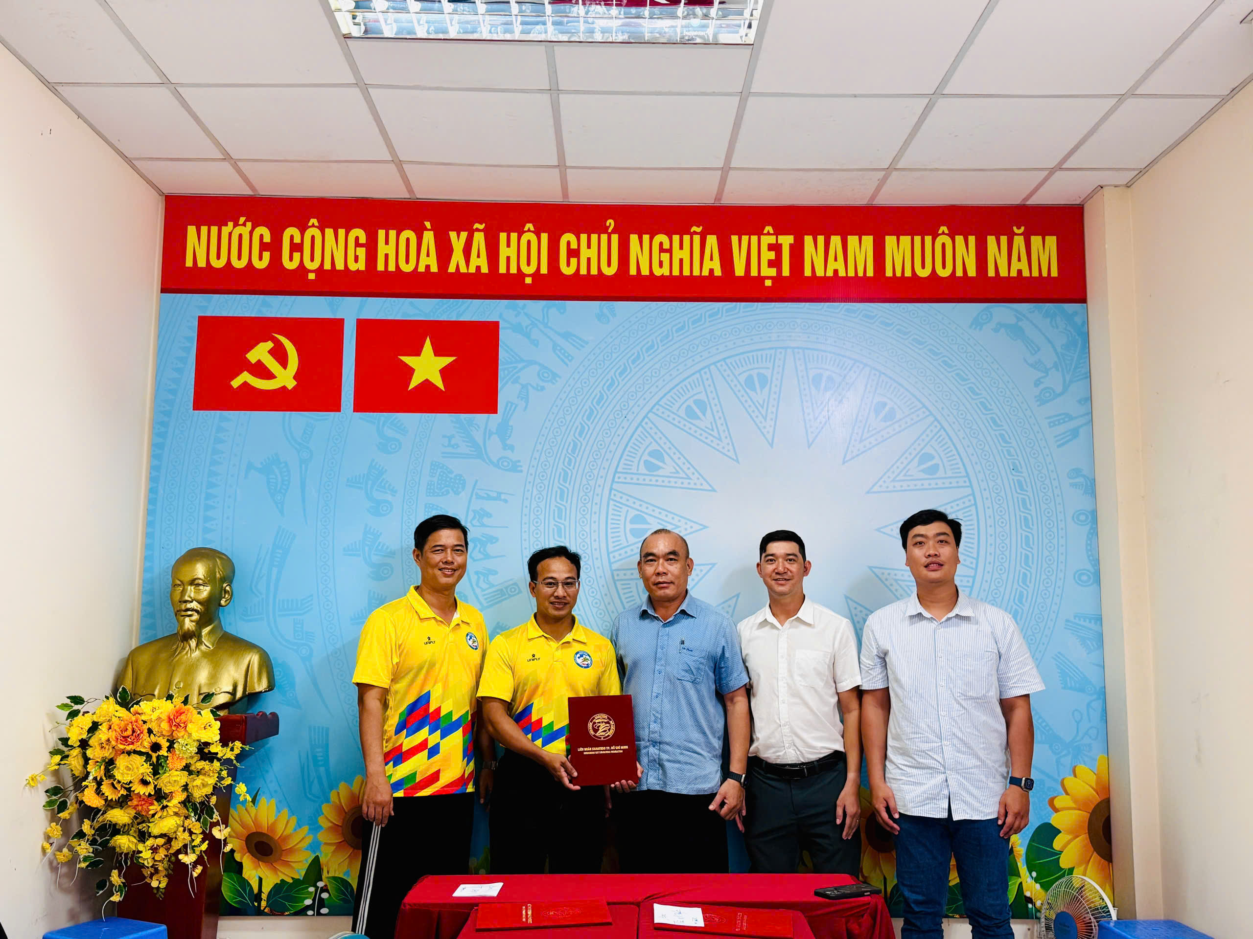 Đại diện Ban Chính sách, Pháp chế và Đối ngoại đứng tại Hội nghị, với một thành viên cầm bìa hồ sơ màu đỏ của HKF.